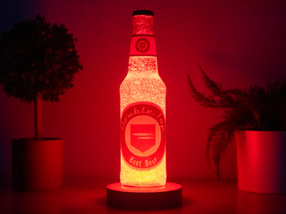The Bottle Light Company’s Double Tap Root Beer Perk a Cola Bottle Light sits on a round base, glowing red. Two potted plants flank it against a dark background, evoking Call of Duty Zombies.