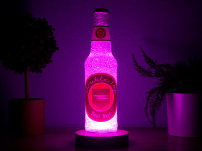 The Double Tap Root Beer Perk a Cola Bottle Light by Bottle Light Company glows with vibrant pink hues between two potted plants, giving off Call of Duty Zombies vibes against a purple-lit background.