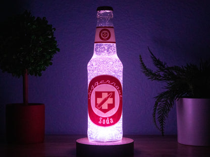The Juggernog Perk a Cola Bottle Light by Bottle Light Company glows with purple LEDs on a wooden base, accented by potted plants against a dark backdrop.