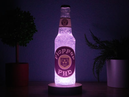 The PHD Flopper Perk a Cola Bottle Light by Bottle Light Company glows softly purple between potted plants—an essential collectible decor piece for any Call of Duty Zombies fan.